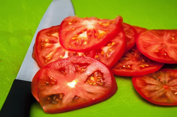 Rode tomaten segmenten en mes op groen hakken bestuur — Stockfoto