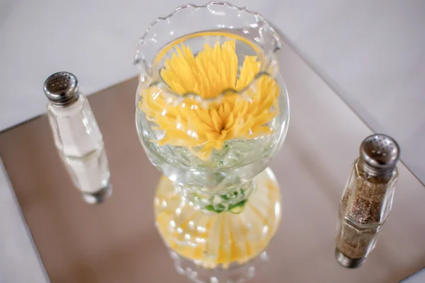 Gele bloemen in glazen kom met zout en peper — Stockfoto