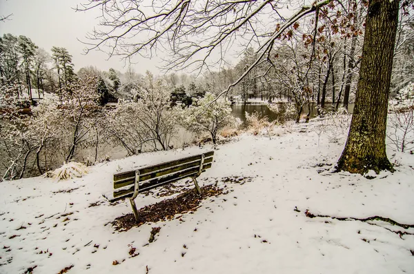 Park bench in the snow covered park overlooking lake — Stock Photo, Image