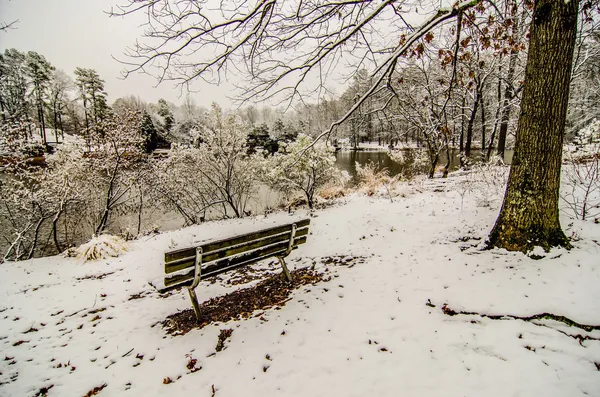 Banco del parque en el parque cubierto de nieve con vistas al lago —  Fotos de Stock