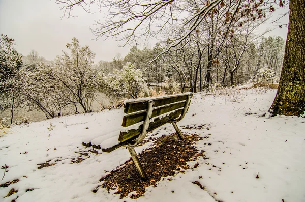 Скамейка в заснеженном парке с видом на озеро — стоковое фото