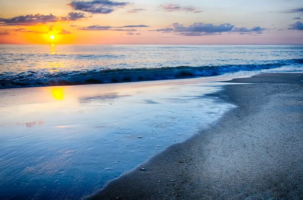 El sol naciente se asoma a través de las nubes y se refleja en olas por —  Fotos de Stock