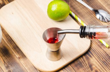 İçki barın şeker kutusuna dökülüyor. Dispanser, şişe, süzgeç ve limon. Tahta bir masanın en üst görüntüsü..