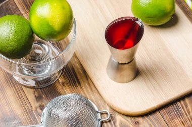 Kırmızı kokteyl yapmak için aletler. Dağıtıcı, süzgeç ve limon. Tahta bir masanın en üst görüntüsü..