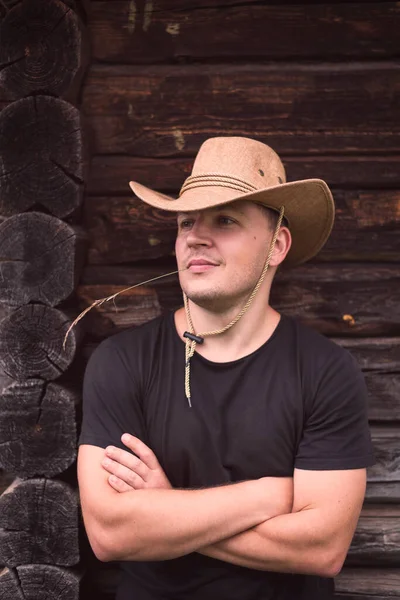 Junger Mann Mit Cowboyhut Auf Dem Hintergrund Eines Holzblockhauses Stockbild
