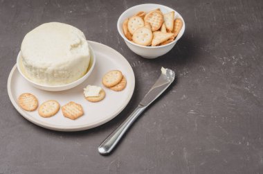 Beyaz kasede peynir ve kraker ve siyah taşlı arka planda bir bıçakla. Boşluğu kopyala.