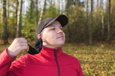 Genç adam maskesini yüzünden çıkardı. Genç adam dışarıda koronavirüsten korunmak için maskesini çıkarıyor.