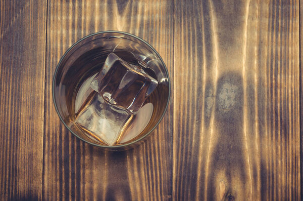 Glass of whiskey with ice on a wooden table. Top view. Transparent glass with alcohol with ice.