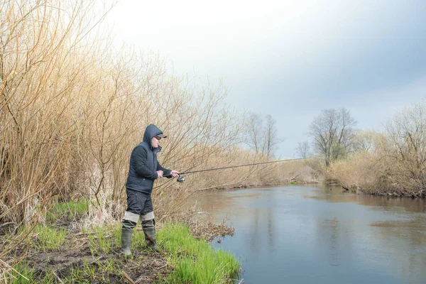 雨の中川のほとりで釣りをする男 — ストック写真