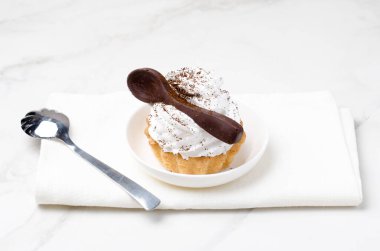 Süslü beyaz protein kremalı kek sepeti beyaz bir tabakta beyaz bir çikolata kaşığıyla süslenmiş. Üst görünüm.