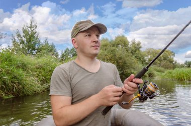 Balıkçı elinde bir değnekle bir kayıkta oturur. Güneşli bir yaz gününde Mutlu balıkçı