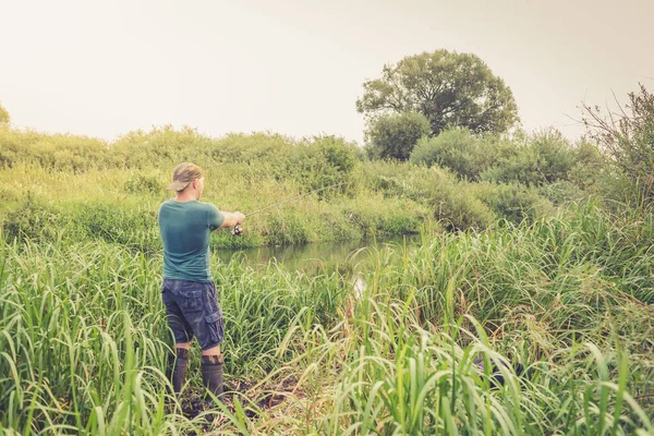 Nehir kıyısında elinde olta olan yakışıklı bir genç. Açık hava sporları.