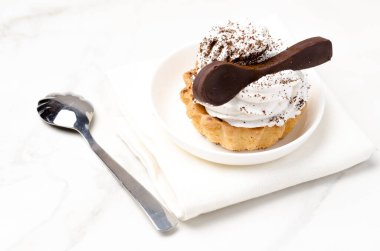 Süslü beyaz protein kremalı kek sepeti beyaz bir tabakta beyaz bir çikolata kaşığıyla süslenmiş. Üst görünüm.