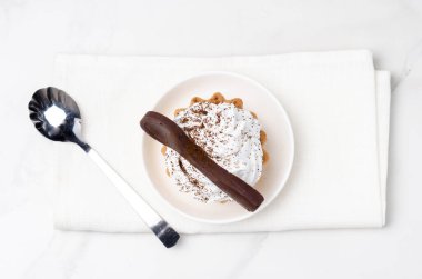 Süslü beyaz protein kremalı kek sepeti beyaz bir tabakta beyaz bir çikolata kaşığıyla süslenmiş. Üst görünüm.