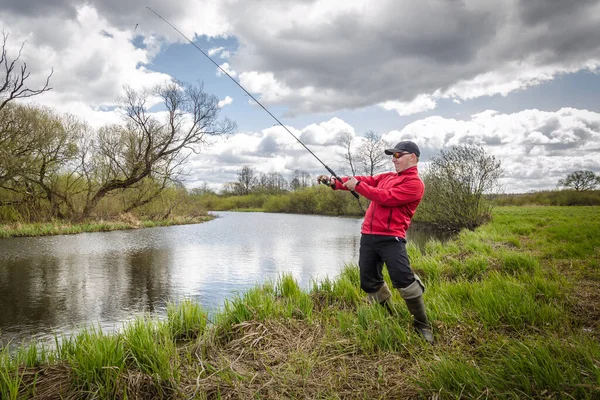 赤い上着を着た漁師が川の緑の岸で釣りをしている 美しい風景 — ストック写真