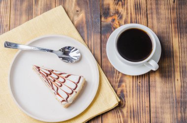 Tahta bir masada bir fincan kahveyle beyaz tabakta cheesecake. Üst görünüm.