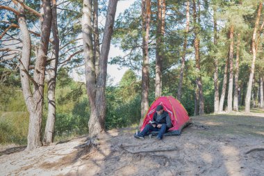 Çadırın yanındaki ormanda oturan adam. Açık hava kampı.