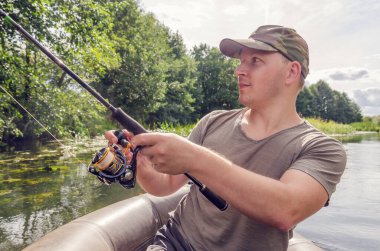 Balıkçı elinde bir değnekle bir kayıkta oturur. Güneşli bir yaz gününde Mutlu balıkçı