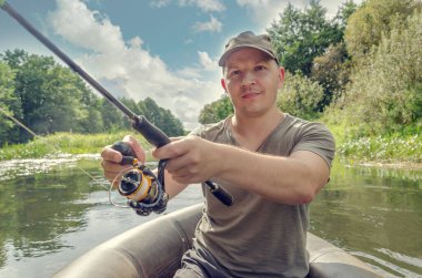 Balıkçı elinde bir değnekle bir kayıkta oturur. Güneşli bir yaz gününde Mutlu balıkçı