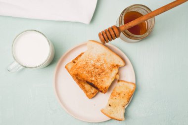 Tabakta tost, kavanozda bir kaşık bal ve bardakta süt. Kahvaltı hala hayattadır. Üst görünüm.