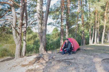 Adam ormanda çadırın yanında oturuyor. Açık hava kampı.