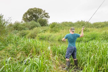 Yakışıklı genç adam nehir kıyısına bir döner çubuk fırlatıyor. Doğadaki hobi.