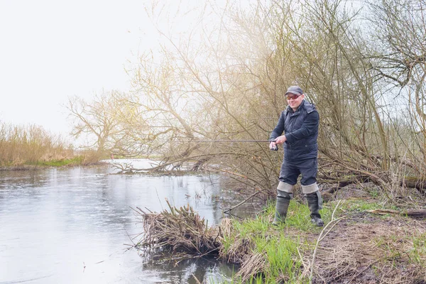 雨の中川のほとりで釣りをする男 — ストック写真