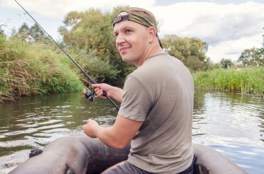 Elinde oltayla bir teknede genç bir balıkçı. Mutlu balıkçı güneşli bir günde.