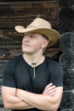 Ahşap bir evin arka planında şapkalı ve siyah tişörtlü bir kovboy..