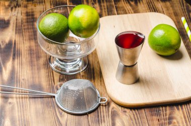 Kırmızı kokteyl yapmak için aletler. Dağıtıcı, süzgeç ve limon. Tahta bir masanın en üst görüntüsü..