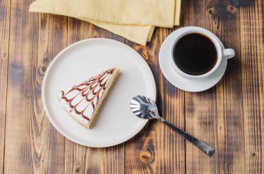 Tahta bir masada bir fincan kahveyle beyaz tabakta cheesecake. Üst görünüm.