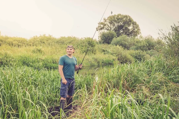 川のほとりに釣竿を持ったハンサムな若い男 アウトドアスポーツ — ストック写真