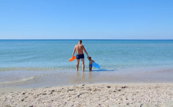 Dad and son with rubber rings walking in the sea and holding hands — Stock Photo, Image