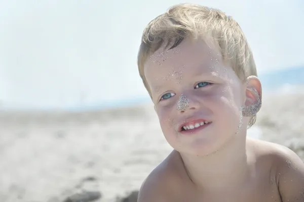 Portrait de garçon de trois ans sur la plage, visage dans le sable — Photo