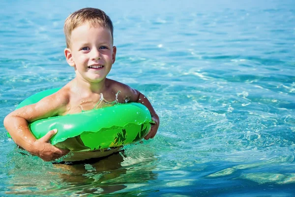 Счастливый мальчик наслаждается купанием в море с резиновым кольцом — стоковое фото