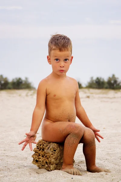 Cute little boy sitting on stone, beach — Stock Photo, Image