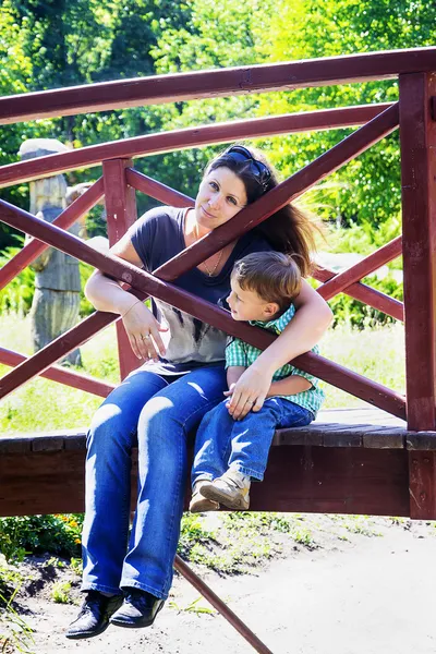 Kleine jongen met zijn moeder zittend op de brug door de vijver — Stockfoto