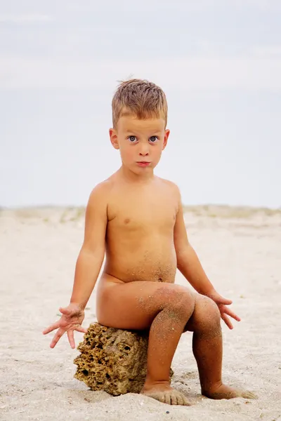 Cute little boy sitting on stone, beach — Stock Photo, Image