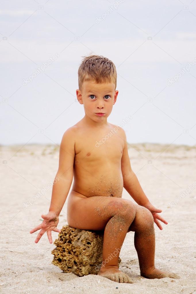 Cute little boy sitting on stone, beach Stock Photo by