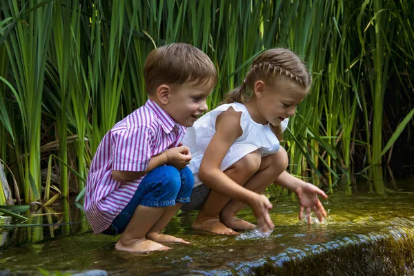 Jongen en meisje zit in water in de buurt van kleine waterval, natte voeten — Stockfoto