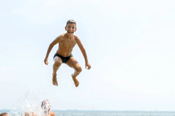 Fericit zece ani băiat sărind în apă pe râu larg din aer. Conceptul de vacanță de vară — Fotografie, imagine de stoc