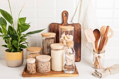 Tahıl çeşitleri, tahıl gevreği ve cam kavanozlarda makarna ve ahşap masada mutfak gereçleri. Sağlıklı dengeli gıda, etik sürdürülebilir yaşam tarzı, sıfır atık, çevre dostu konsept.