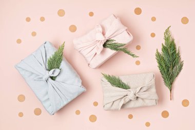 Geleneksel Japon furoshiki tarzını pembe zemine saran sıfır atık hediyesi. Plastiksiz, el yapımı Noel, doğum günü, Paskalya ve diğer şenlikli etkinlikler için hediye paketi