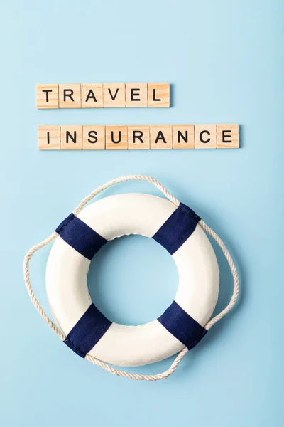 Safe travel, protection tourism insurance concept. Travel insurance wooden letters and lifebuoy over blue background. Top view, flat lay.