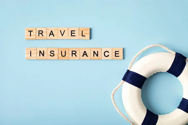 Safe travel, protection tourism insurance concept. Travel insurance wooden letters and lifebuoy over blue background. Top view, flat lay.