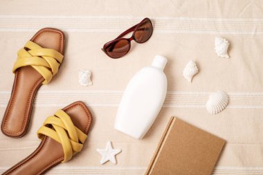 Yaz tatilleri plaj aksesuarlarıyla dolu. Terlikler, güneş kremi, plaj havlusunun üzerindeki deniz kabukları seyahat, turizm konsepti. Üst görünüm