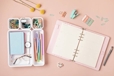 Pembe arka planda merkez ofis masaüstü. Not defterli modern çalışma alanı, plastik organizatörlerde ofis sabit