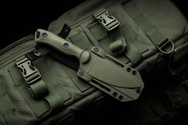 Modern bir askeri bıçak ve plastik bir kılıf. Sivri uçlu silahlar, askeri zeytin rengi bir sırt çantasının üzerinde..