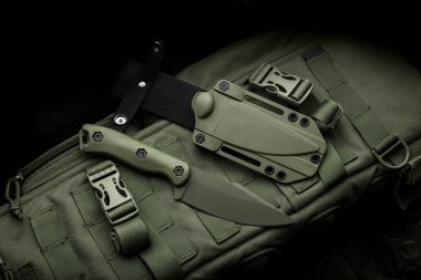 Modern bir askeri bıçak ve plastik bir kılıf. Sivri uçlu silahlar, askeri zeytin rengi bir sırt çantasının üzerinde..