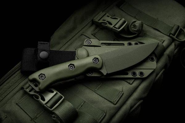 A modern military knife and a plastic sheath for it. Edged weapons lie on a military olive-colored backpack.